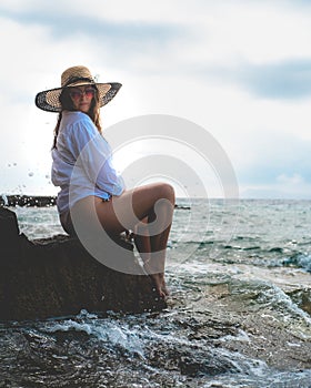Side view of an amazing brunette sitting on a rock by the sea. Beautiful teal adriatic sea on the island of Vis, summer of 2021.
