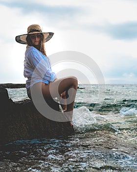 Side view of an amazing brunette sitting on a rock by the sea. Beautiful teal adriatic sea on the island of Vis, summer of 2021.