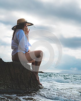 Side view of an amazing brunette sitting on a rock by the sea. Beautiful teal adriatic sea on the island of Vis, summer of 2021.