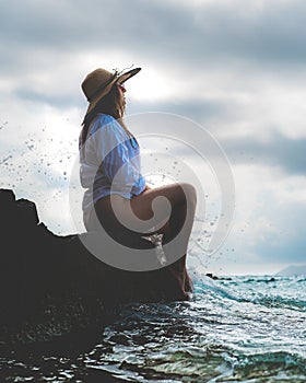 Side view of an amazing brunette sitting on a rock by the sea. Beautiful teal adriatic sea on the island of Vis, summer of 2021.