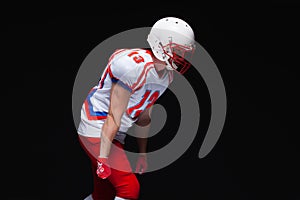 Side view of American football player wearing helmet taking position while playing against black background