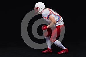 Side view of American football player wearing helmet taking position while playing against black background