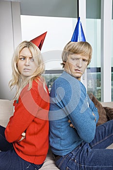 Side view of annoyed couple in Christmas sweaters and party hats sitting back to back at home