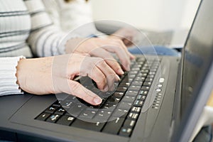 Side view of anonymous woman in casual clothes typing on laptop keyboard while working on freelance work at home