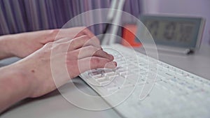 A side view as women's hands type on a white computer keyboard.