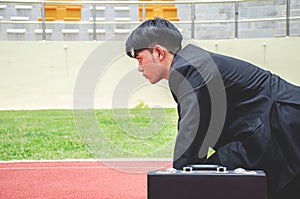 Side view of Asian business man ready to run on the lanes of a track