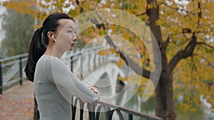 Side View of the Asian Female Runner Enjoying Outside Listening to Music. Jogger Woman After Running Resting in the