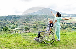 Side view of Asian nurse and senior man on wheelchair action of stretching together and both stay near the cliff with mountain and