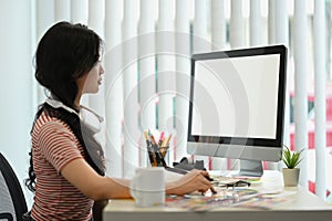 Side view of asian woman looking at computer monitor, working on designer project in creative office