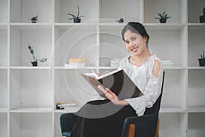 Side view of asian woman sitting armchair with open book and reading