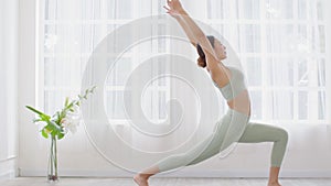 Side view of Asian woman wearing green sportwear doing Yoga exercise in front of windows,Yoga high lunge pose or Anjaneyasana,Calm