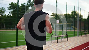 Side view of an athlete is running on race track on athletics stadium in black shirt