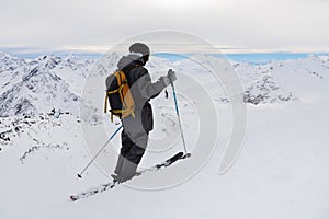 Side view of an athletic skier in a helmet and goggles with a backpack, standing on skis, holding ski poles in white