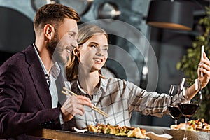 Side view of attractive couple taking selfie during dinner