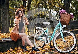 Happy woman sitting near bicycle in urban autumn park.