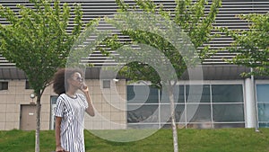 Side view of attractive young smiling african american business woman in sunglasses talking on cellphone while waiting