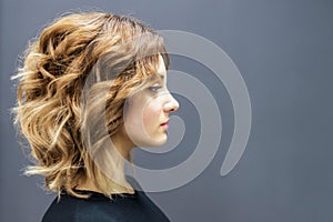 Side view of attractive young woman with curly hair standing against grey isolate.