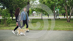 Side view of attractive young woman dog owner walking her pet and chatting to her boyfriend going hand in hand with her