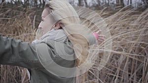 Side view of attractive young woman standing in wind. Blond Caucasian girl enjoying grey autumn day outdoors.