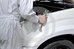 Side view of automotive mechanic in uniform with wrench diagnosing engine under hood of car at the repair garage.