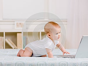 Side view of baby crawling in bed toward laptop