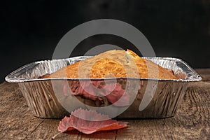 Side view of a baked pie in the form of thick aluminum foil on a wooden table