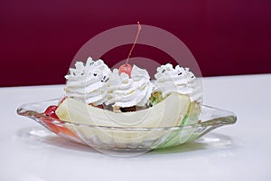 Side view Banana Split Ice Cream in a boat shaped glass cup on white table background,red wall background,food, copy space