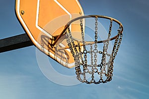 Side view of Basketball backboard with the hoop metal ring and steel chain net against blue sky background seen from below
