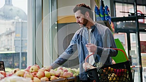 Side view of bearded male shopping fresh apples in supermarket setting