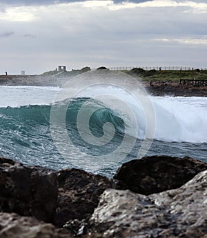 Side view of a beautiful clear wave that is just flipping and falling into the rest of the sea and crashed against cliffs and