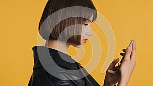 Side view of beautiful girl with bob hair surfes social media on smartphone isolated on yellow background