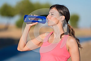 Side view of beautiful girl in sport clothes drinking water after workout on the park