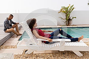 Woman relaxing on a sun lounger while man using mobile phone in the background