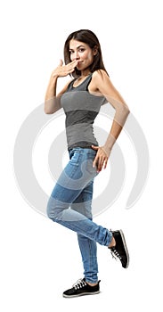 Side view of beautiful woman in gray top and blue jeans standing with one hand covering mouth and one knee bent and foot