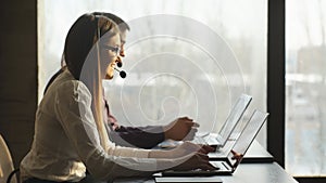 Side view of beautiful young business woman and handsome businessman in headsets using laptops while working in office.