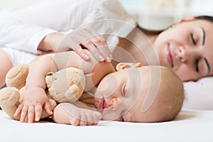 Side view of beautiful young mom and her cute baby sleeping in bed at home