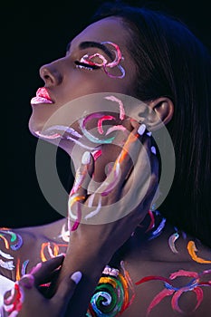 Side view on beautiful young woman with fluorescent prints on skin