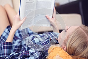 Beautiful young woman laying on the floor at home, reading a book, living room interior. Girl reading a book on the
