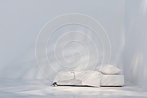 Side view of bed with white linen. Light and shadows on white wall