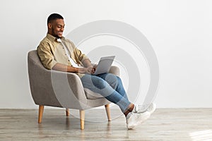Side-View Of Black Freelancer Man Using Laptop Working Online Indoors
