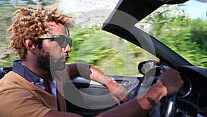 Side view of black man driving convertible car through traditional old town