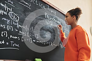 Side view black teenage girl writing on blackboard in school classroom