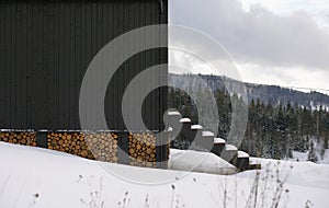 Side view of black wooden house with stacked firewood under