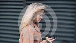 Side view of blonde woman with coffee walking and web surfing