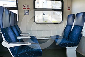 Side view of blue armchairs in empty train in row of three, no people in wagon, comfortable way of transportation,