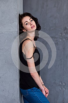 Side view of blue-eyed brunette with full lips and pale complexion leaning against wall turned head to camera