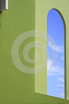 Side view of blue sky inside of open exterior window arch frame on green concrete wall of vintage house building