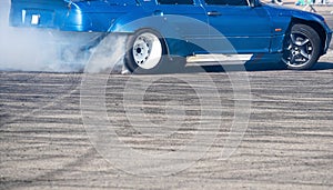 side view of blue sport car drifting on gray speed tarmac track with smoke coming out of the back tire wheel