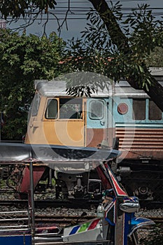 Side view of Blue Tuk Tuk 3-wheeler taxi and Diesel electric locomotive is parked overlapping