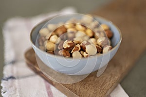 Side view of bowl of hazelnuts on wood board with a napkin in the background